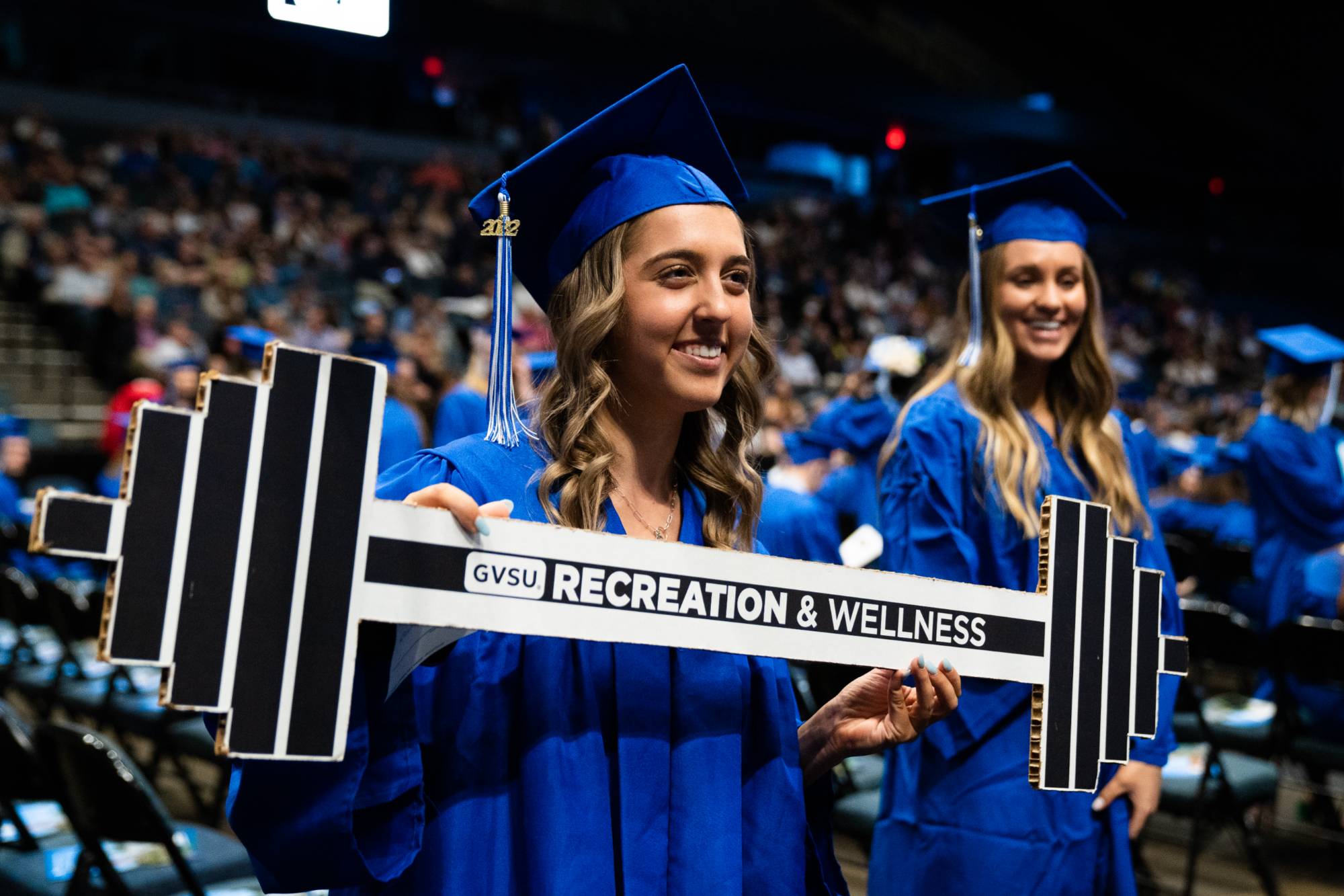 student at commencement holding and rec & wellness sign